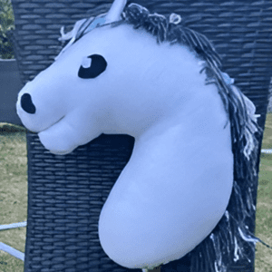 The Vestibulum Dictum, a plush hobby horse with a white head and black mane, is set against a woven basket backdrop.