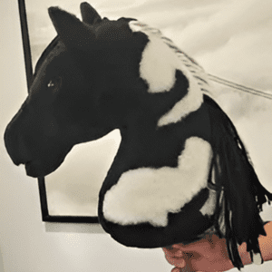 The "Vestibulum Dictum" is a plush hobby horse in black and white, featuring a fringed mane, showcased indoors against a monochrome background.