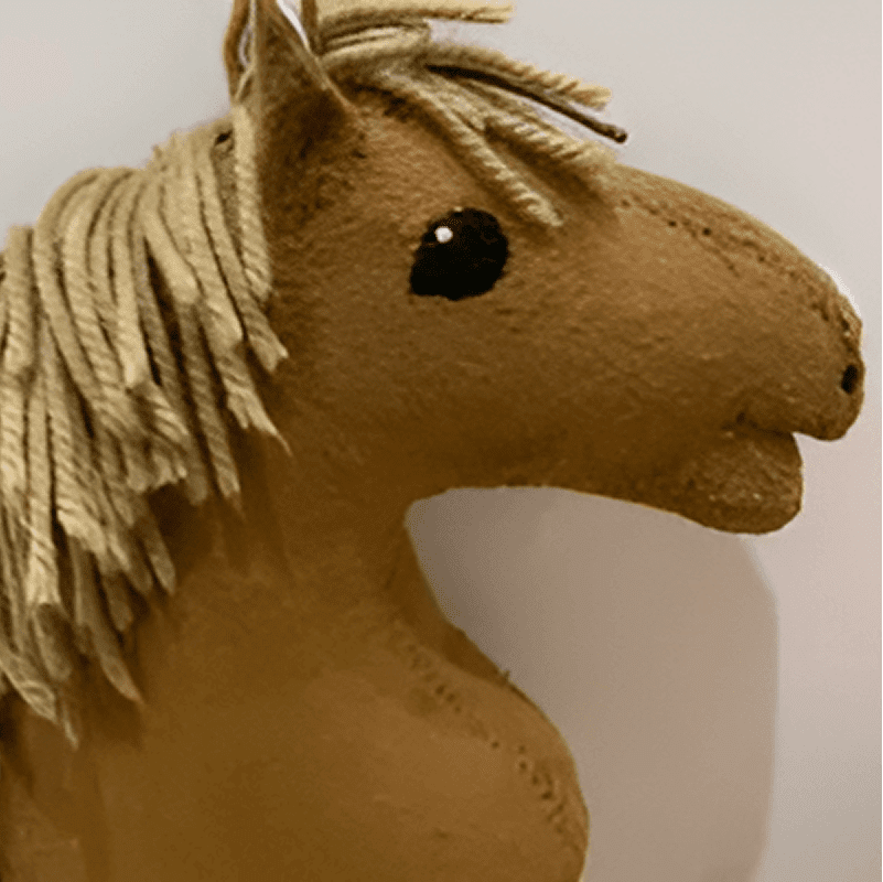 A handmade felt horse toy with beige fabric, yarn mane, and black stitched eyes.