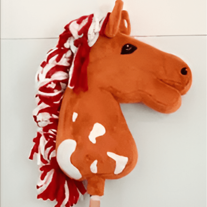 Plush toy horse head with a red and white mane and brown spotted body, mounted on a stick against a plain background.