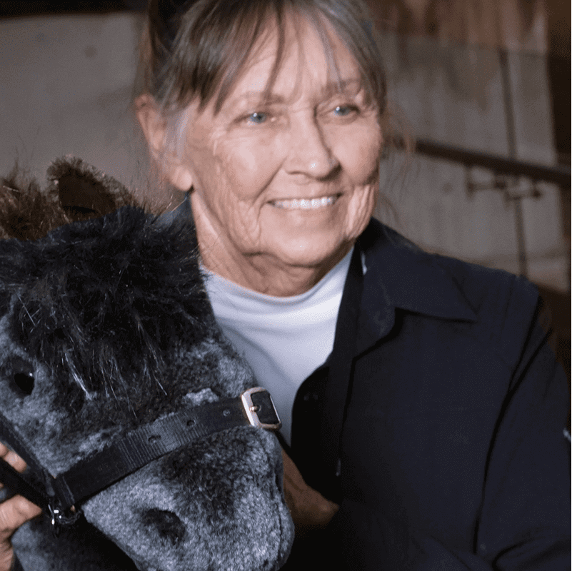 An older woman smiling while holding a plush horse toy.