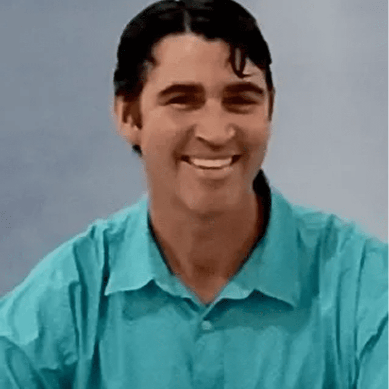 A person with dark hair is smiling, wearing a turquoise shirt, against a plain background.