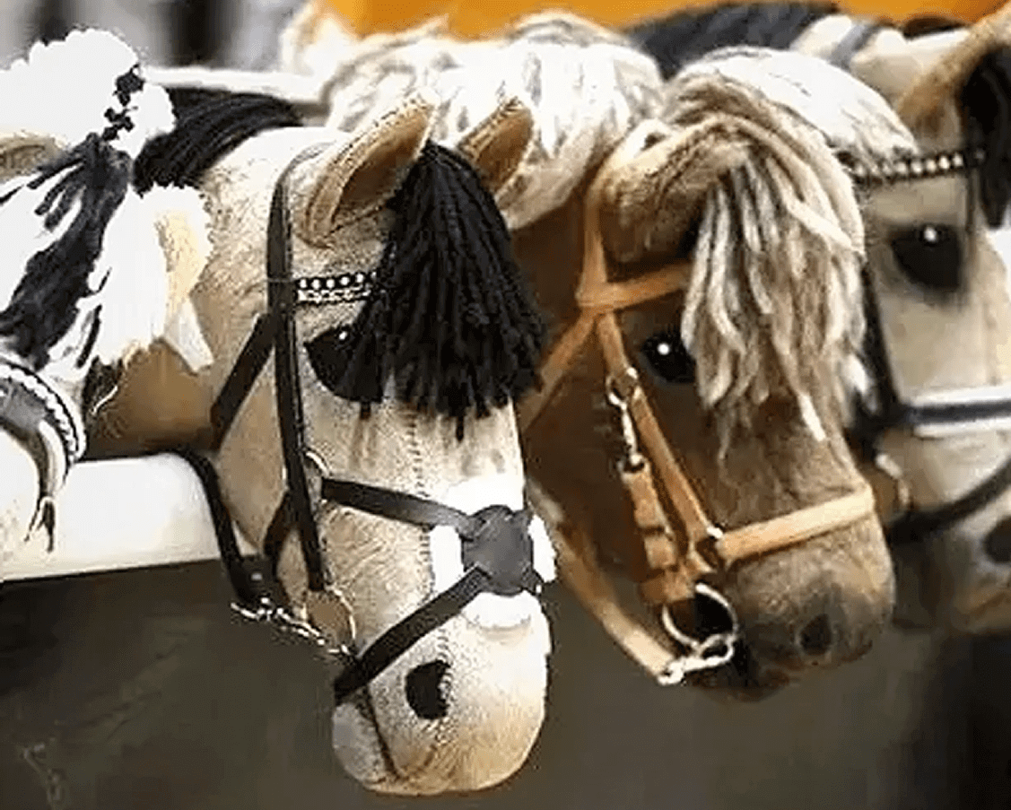 Several plush hobby horses with various colored manes and bridles are lined up side by side.