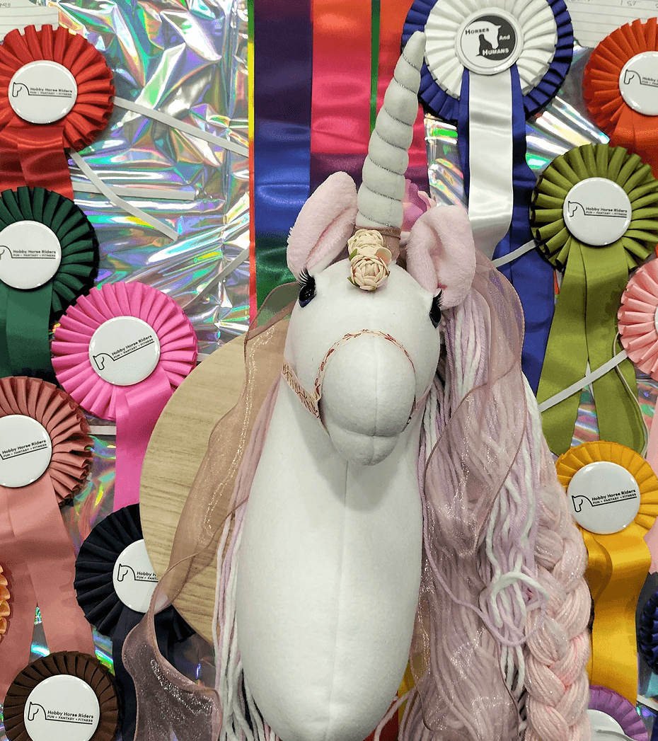 Unicorn plush with pastel mane surrounded by various colorful award ribbons on a holographic background.