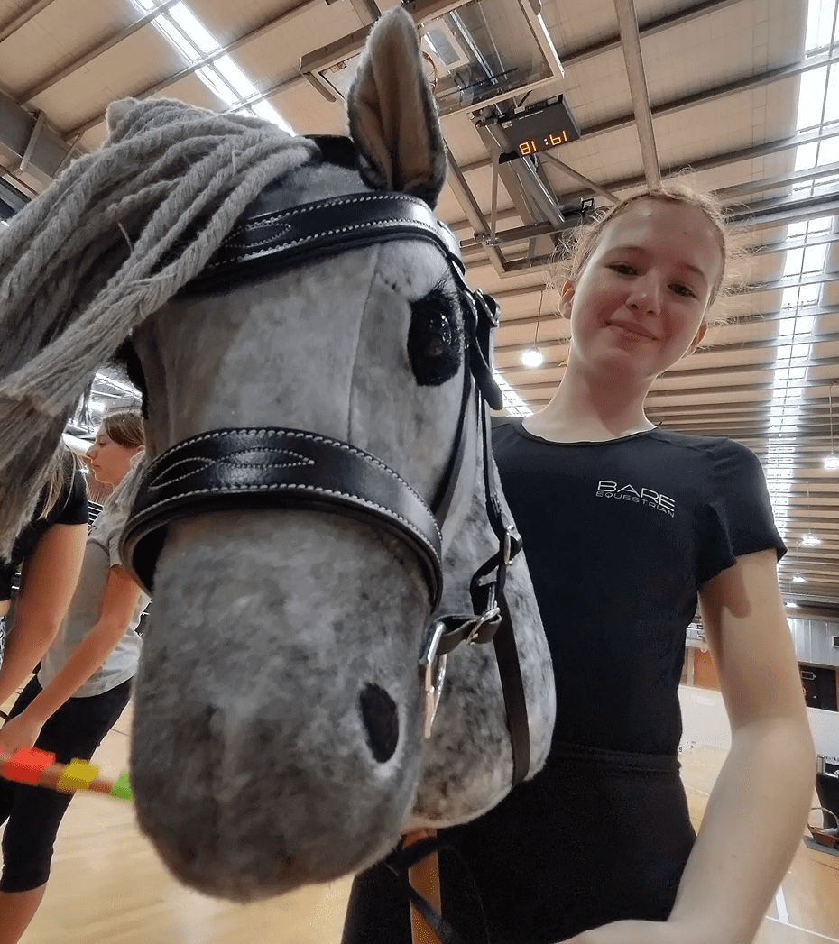 A person holds a gray hobby horse indoors, smiling at the camera.