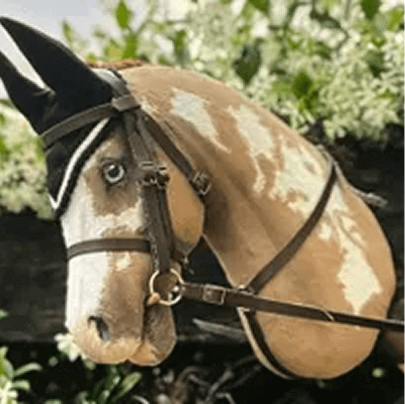 A realistic toy horse head with a bridle, against a leafy background.