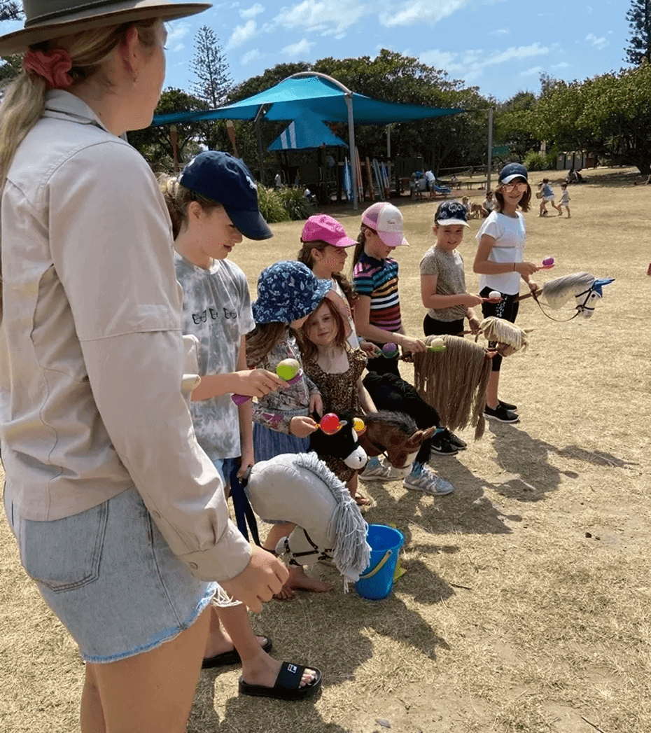 Children playing with hobby horses outdoors.