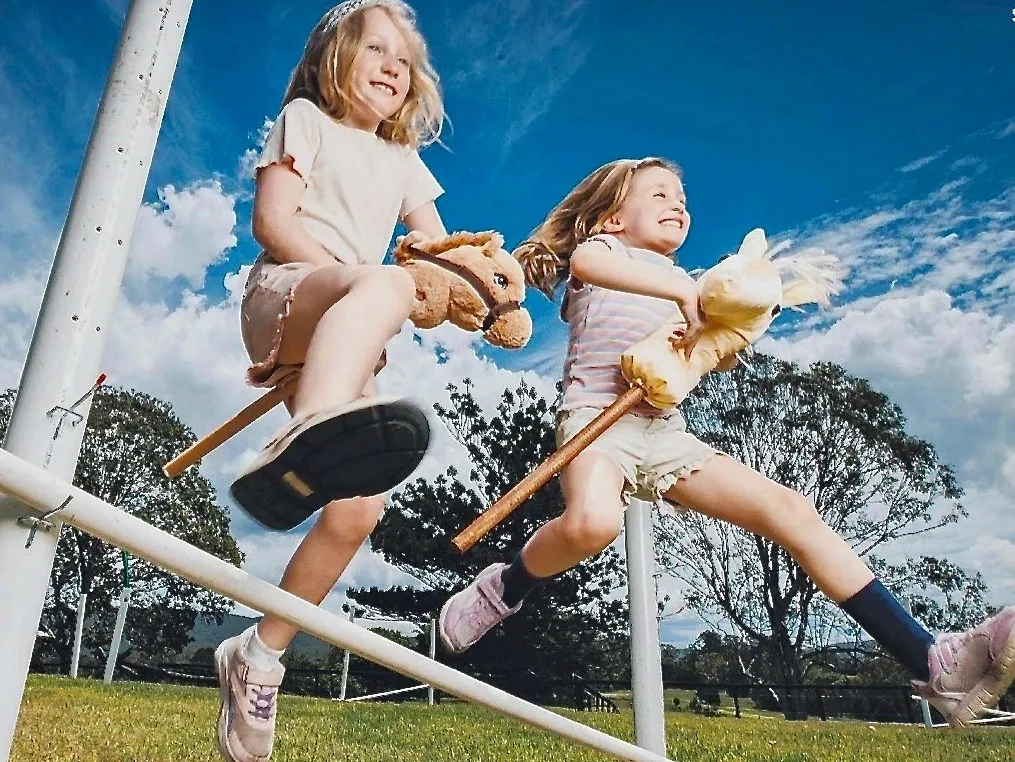 Two girls playing and jumping over a railing outdoors on a sunny day.