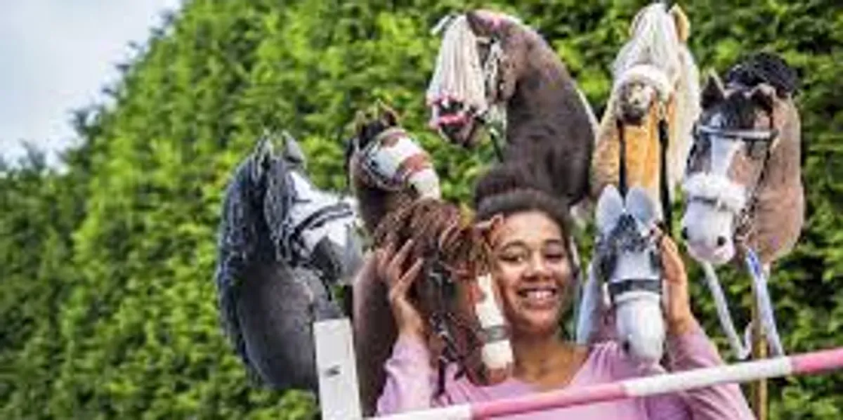 Smiling woman holding a small brown horse toy with larger horse toys in the background.