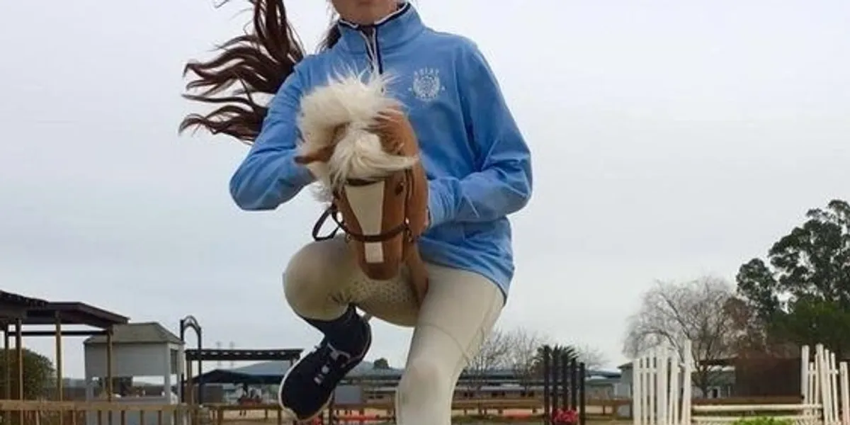 Person jumping over a hurdle while holding a toy horse.