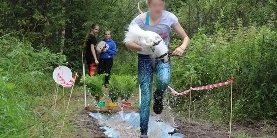 Woman running in a muddy outdoor race with a dog in her arms.