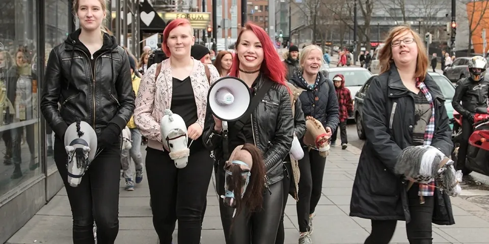 Two women lead a street protest, one holding a megaphone and a horse mask.