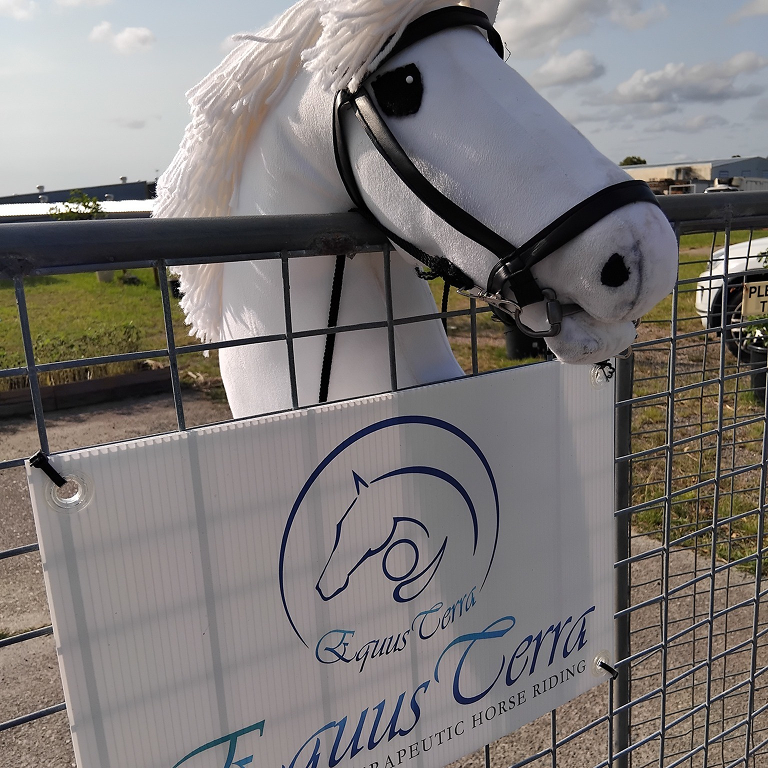 A realistic white horse head model behind a sign at an outdoor event.