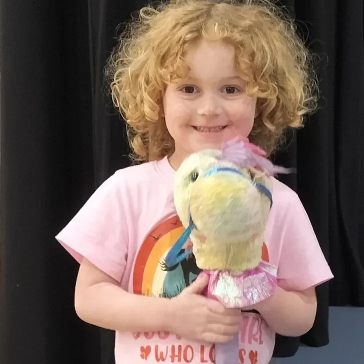 Smiling child holding a colorful plush toy.