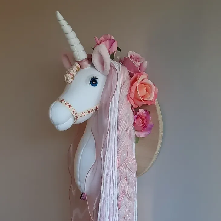 Crafted unicorn head with floral and ribbon decorations on a wall.